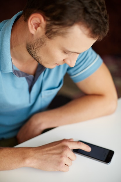 Jeune homme en chemise bleue, surfant sur le téléphone, les réseaux sociaux discutant sur Internet