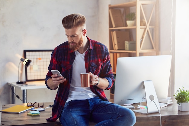 Jeune homme en chemise à carreaux tenant un smartphone et une tasse de café