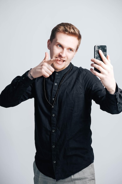 Jeune homme en chemise noire avec un smartphone dans ses mains sur un fond blanc
