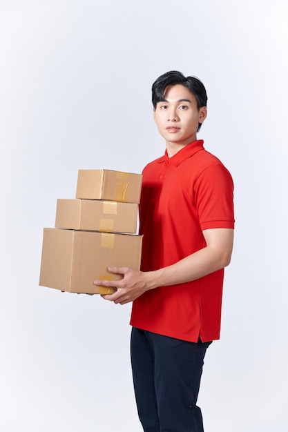 Jeune homme en chemise rouge portant trois boîtes en carton sur un mur blanc