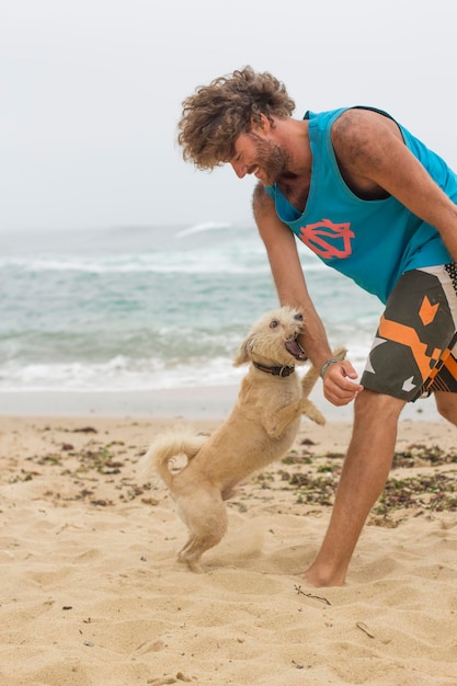 Un jeune homme avec un chien qui joue sur la plage.