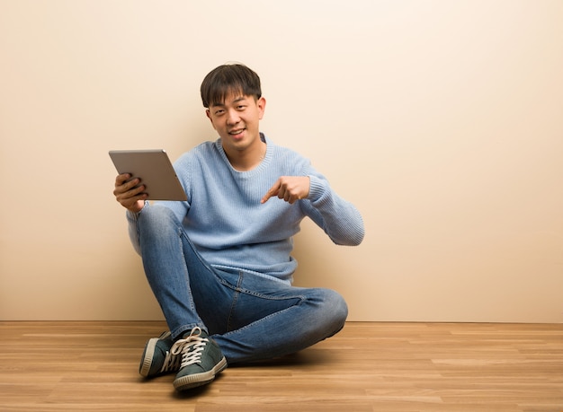 Jeune homme chinois assis à l'aide de sa tablette pointant vers le bas avec les doigts