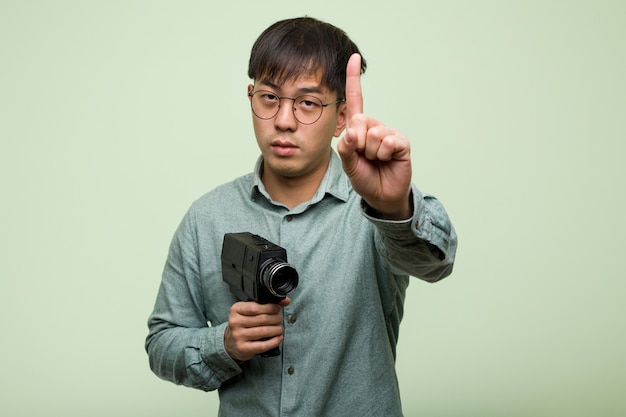 Jeune homme chinois tenant un appareil photo vintage montrant le numéro un