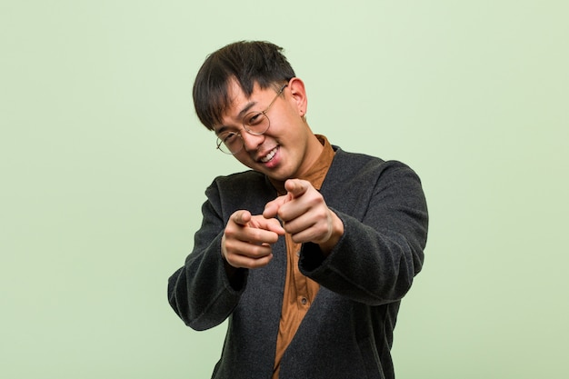 Jeune homme chinois vêtu d'un style de vêtements cool contre un mur vert