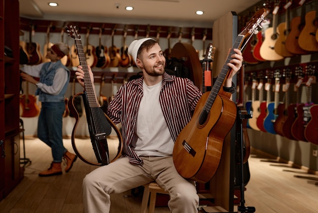 Jeune homme choisissant entre guitare acoustique et électrique. Guitariste du millénaire achetant un nouvel instrument dans un magasin de musique