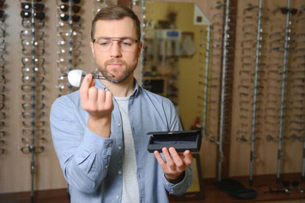 Jeune homme choisissant des lunettes au magasin d'optique