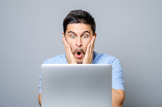 Jeune homme choqué en chemise bleue à l'aide d'un ordinateur portable