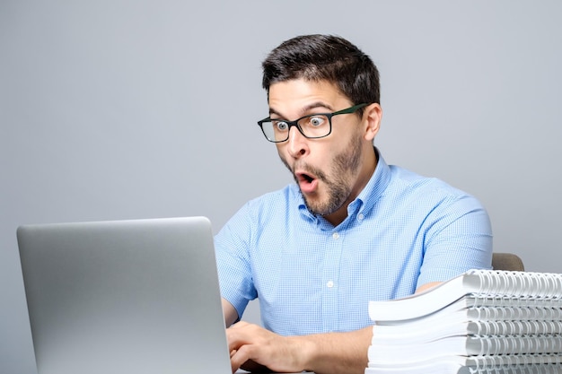 Jeune homme choqué en chemise bleue à l'aide d'un ordinateur portable