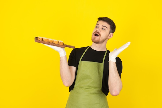 Jeune homme choqué tenant un tas de tranches de gâteau sur un plateau en bois.