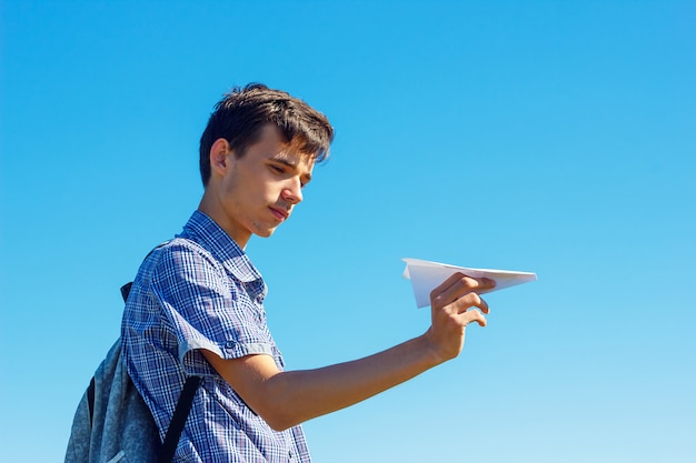 Un jeune homme sur un ciel bleu tenant un avion en papier