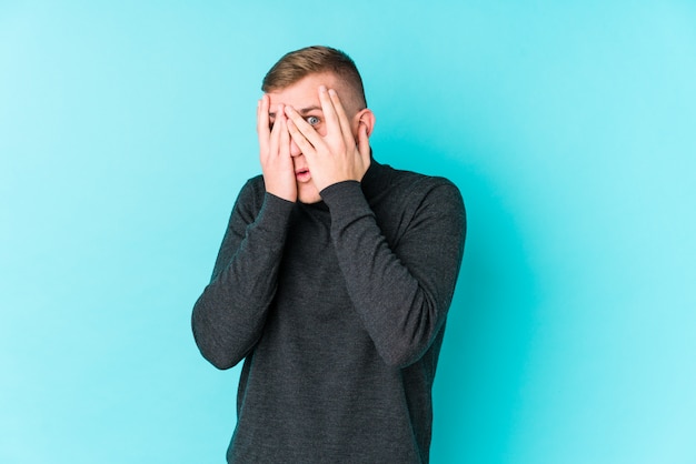 Jeune homme sur un clin d'œil bleu entre les doigts effrayé et nerveux.