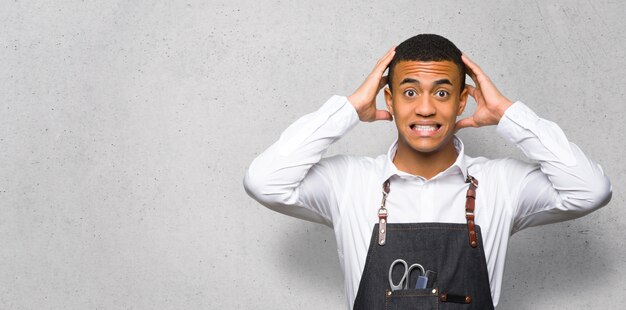 Jeune homme de coiffeur afro-américain prend les mains sur la tête car a la migraine sur le mur texturé