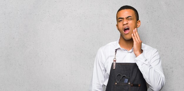 Jeune homme de coiffeur américain afro avec maux de dents sur le mur texturé