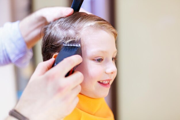 Le jeune homme le coiffeur coiffe le garçon Il coupe les cheveux à l'aide d'une tonte