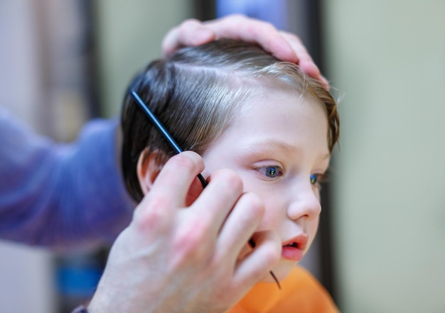 Le jeune homme le coiffeur coiffe le garçon Il coupe les cheveux avec des ciseaux