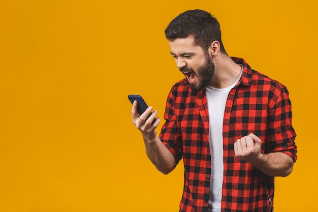 Jeune homme en colère criant sur le téléphone portable isolé sur un mur jaune.