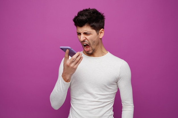 Jeune homme en colère parlant au téléphone à l'aide de son microphone criant regardant vers le bas isolé sur fond violet