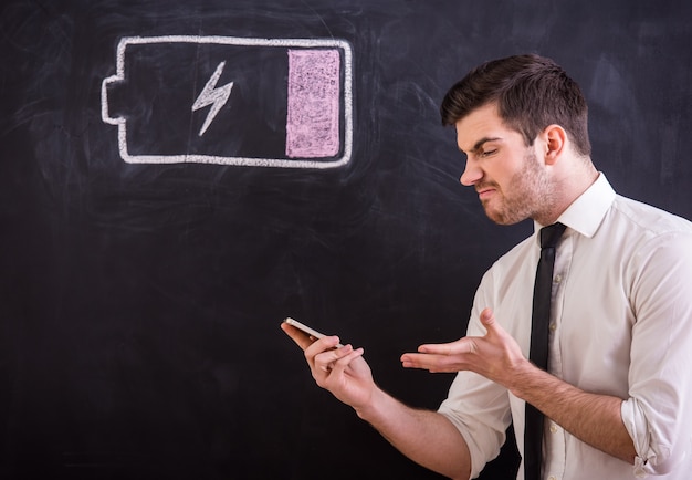 Jeune homme en colère tient son smartphone avec batterie faible.