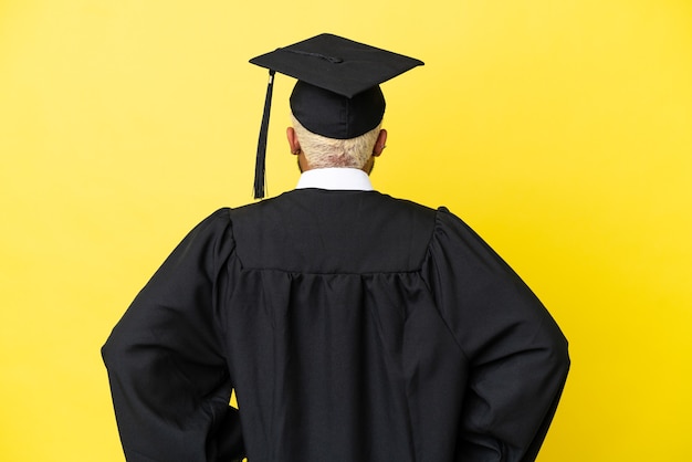 Jeune homme colombien diplômé universitaire isolé sur fond jaune en position arrière