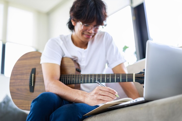 Jeune homme compositeur composant une chanson avec guitare et ordinateur portable à la maison Mise au point sélective de la main du musicien