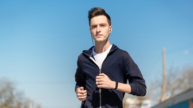 Jeune homme concentré en cours d'exécution avec écouteurs et bracelet de remise en forme, veste.