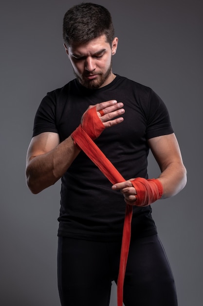 Jeune homme concentré enveloppant les mains avec du ruban de boxe