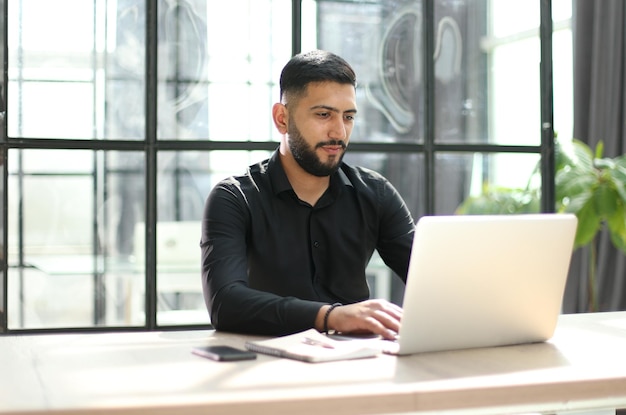 Jeune homme concentré portant à l'aide d'un ordinateur portable sur le clavier écrivant un e-mail ou un message