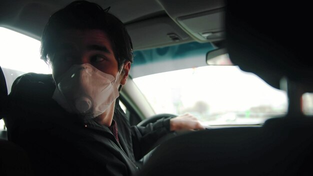 Jeune homme conducteur inexpérimenté portant un masque de protection conduisant une voiture et regardant en arrière
