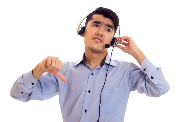 Jeune homme confiant aux cheveux noirs en chemise bleue avec un casque noir montrant le pouce vers le bas