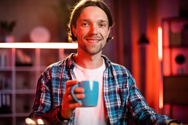 Jeune homme confiant buvant du café ou du thé ou une boisson chaude au bureau
