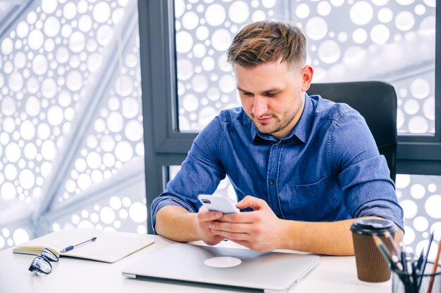 Un jeune homme confiant dans des vêtements décontractés élégants tient un smartphone au bureau