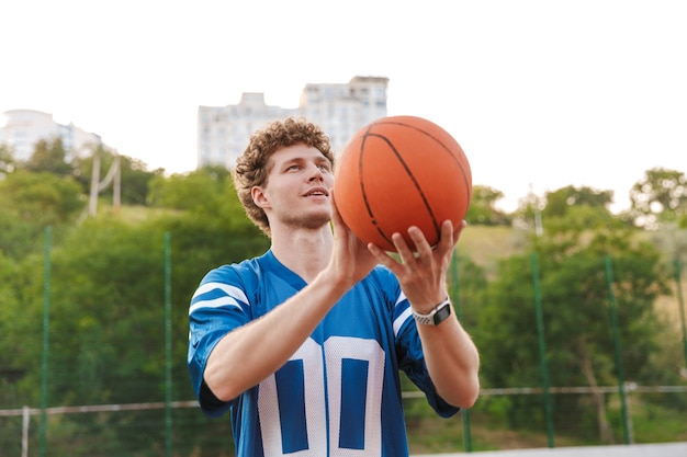 Un jeune homme confiant jouant au basket est sur le point de lancer la balle dans le filet en se tenant debout sur le terrain de jeu