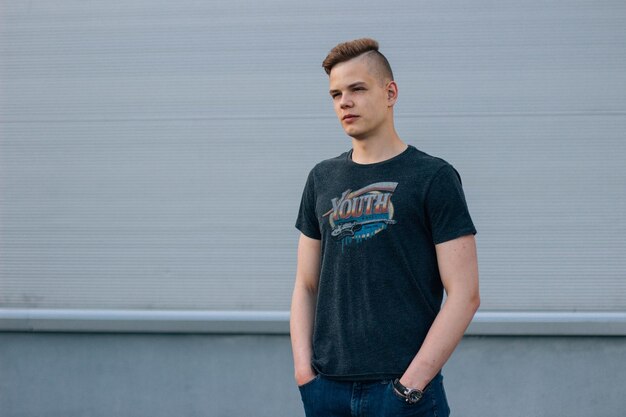 Un jeune homme confiant avec les mains dans les poches debout contre le mur.