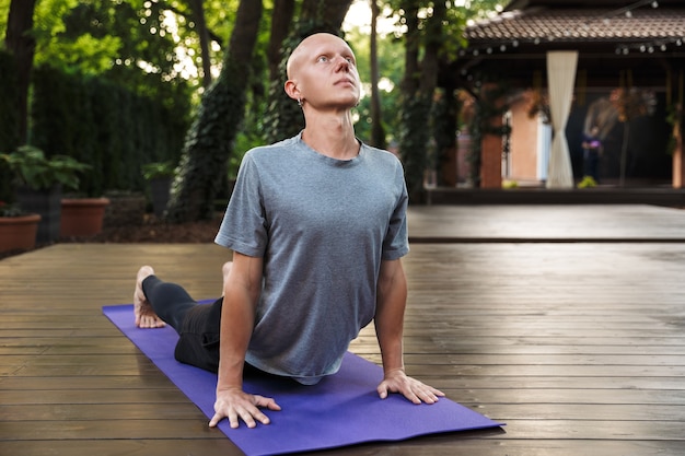 Jeune homme confiant de remise en forme faisant des exercices d'étirement de yoga sur un tapis à l'extérieur