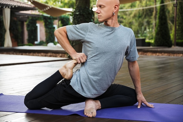 Jeune homme confiant de remise en forme faisant des exercices d'étirement de yoga sur un tapis à l'extérieur