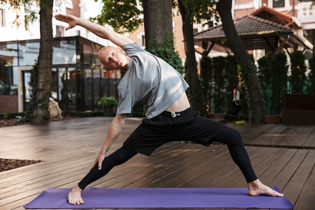 Jeune homme confiant de remise en forme faisant des exercices d'étirement de yoga sur un tapis à l'extérieur