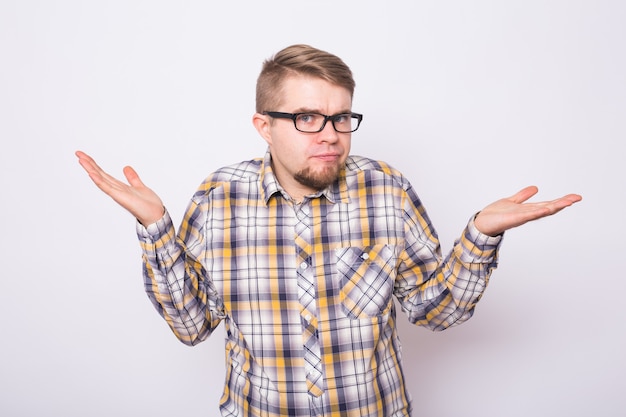 Jeune homme confus habillé en chemise debout sur fond blanc, gesticulant des mains.