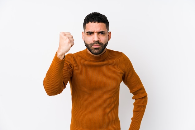 Jeune homme contre un blanc montrant le poing à la caméra, une expression faciale agressive.