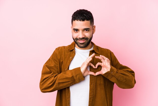 Jeune homme contre un sourire rose et montrant une forme de coeur avec les mains.