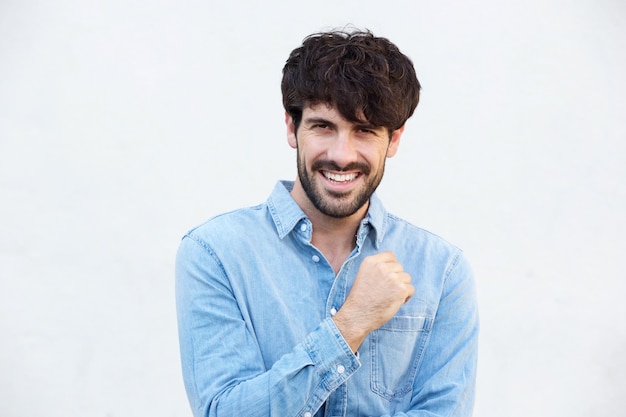 Un jeune homme cool avec une barbe souriant contre le mur blanc