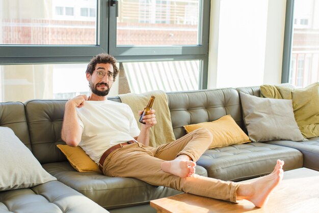 Jeune homme cool barbu assis sur un canapé à la maison