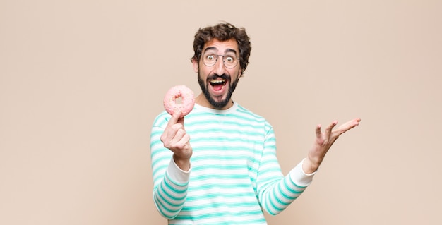 Jeune homme cool avec un beignet rose sucre sur le mur