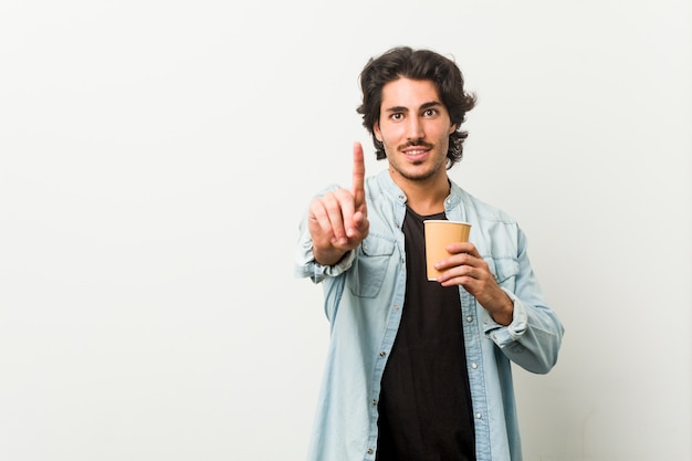 Jeune homme cool, boire un café montrant le numéro un avec le doigt.