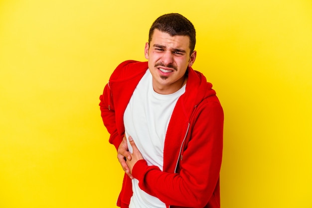 Jeune homme cool caucasien isolé sur fond jaune ayant une douleur au foie, mal à l'estomac.