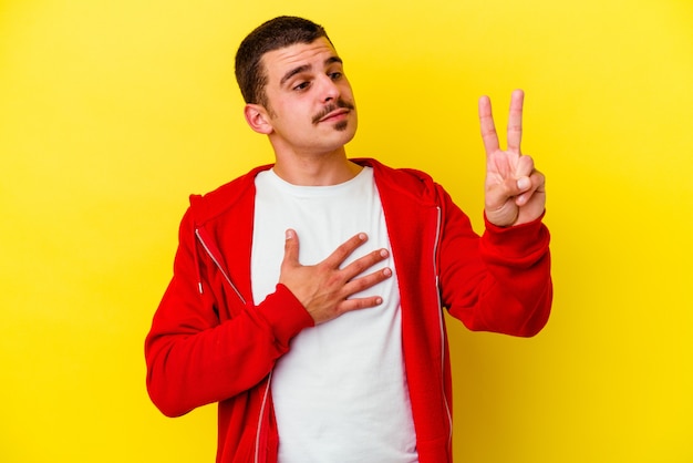 Jeune homme cool caucasien isolé sur fond jaune prêtant serment, mettant la main sur la poitrine.