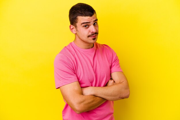 Jeune homme cool caucasien isolé sur un mur jaune malheureux à la recherche à huis clos avec une expression sarcastique.