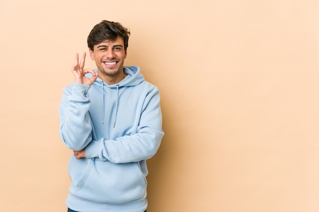 Jeune homme cool fait un clin d'œil et tient un bon geste avec la main