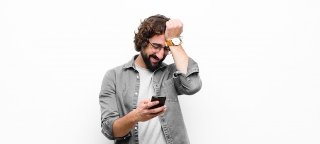 Jeune homme cool fou à l'aide de son smartphone contre le mur blanc