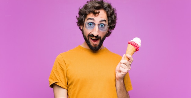 Jeune homme cool fou ayant une crème glacée contre le mur violet