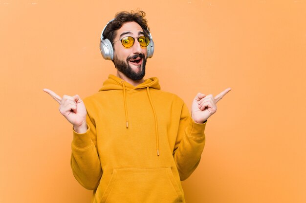 Jeune homme cool fou, écouter de la musique avec des écouteurs contre le mur orange